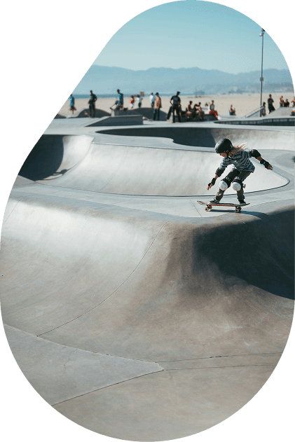 A young skateboarder carving through a concrete bowl at an outdoor skatepark